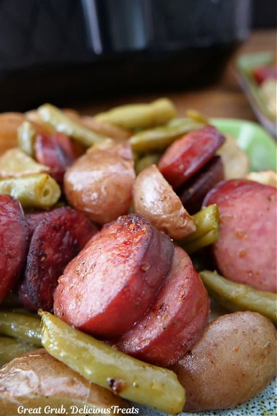 A serving of sausage, potatoes, and green beans on a green square plate.