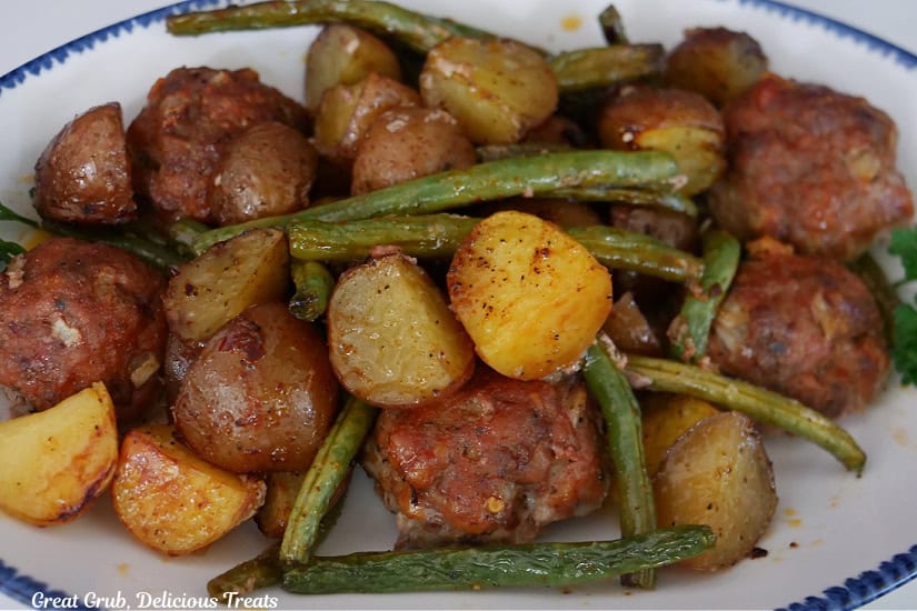 A white oval plate with blue trim with a serving of meatballs, potatoes, and green beans.