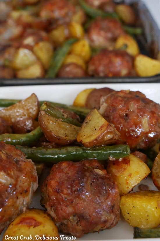 A white plate with a serving of potatoes, green beans and meatballs with the sheet pan in the background.