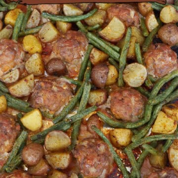A baking sheet with homemade meatballs, potatoes, and green beans on it.