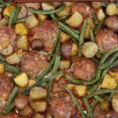 A baking sheet with homemade meatballs, potatoes, and green beans on it.