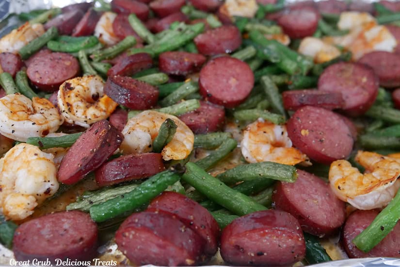 A sheet pan filled with green beans, shrimp, and sliced smoked sausage.
