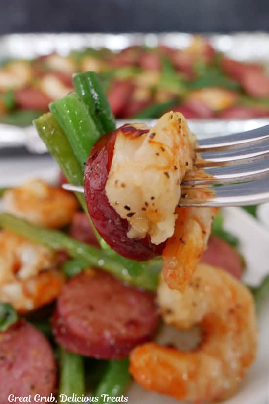 A fork with shrimp, sausage, and green beans on it.