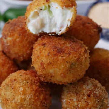 A small round white plate with blue trim with a stack of shrimp poppers on it with a bite out of the popper on top.