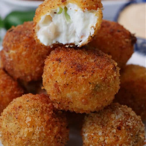 A small round white plate with blue trim with a stack of shrimp poppers on it with a bite out of the popper on top.