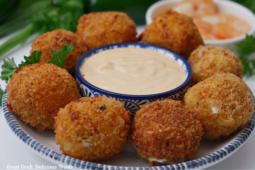A round white plate with blue trim with eight shrimp poppers on it with a small blue bowl filled with dip in the center.