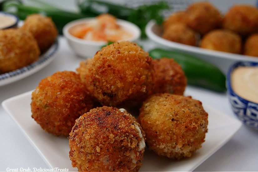 A small square whit plate with 5 shrimp poppers on it with other small plates filled with more poppers.