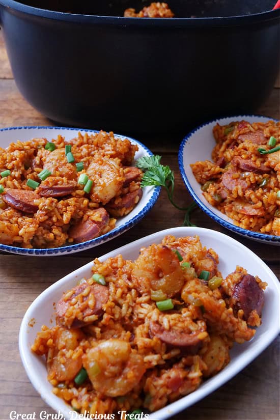 A wood surface with three white bowls filled with shrimp and sausage jambalaya.