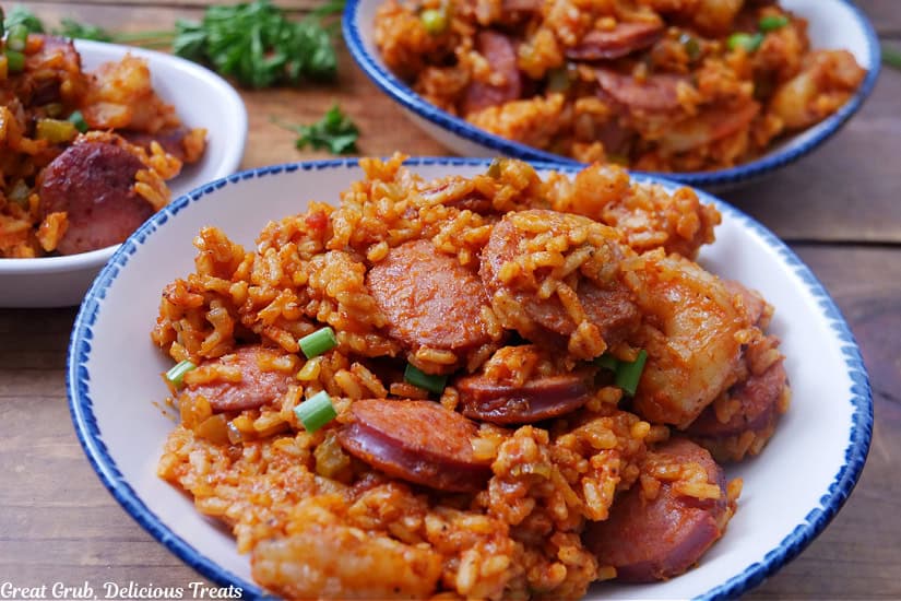 A wood surface with three white bowls with a hearty serving of jambalaya with sausage and shrimp.