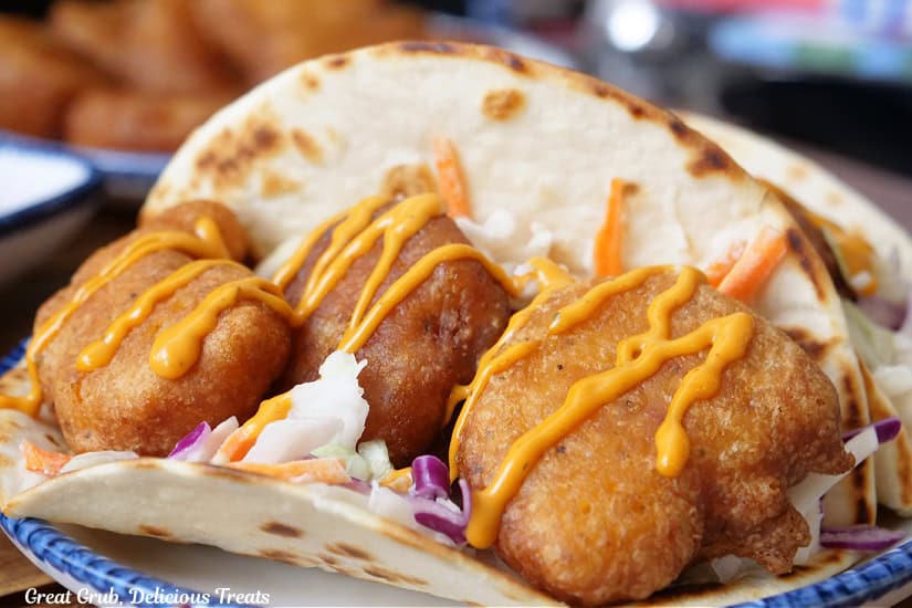 A white plate with blue trim with two shrimp tacos on it.