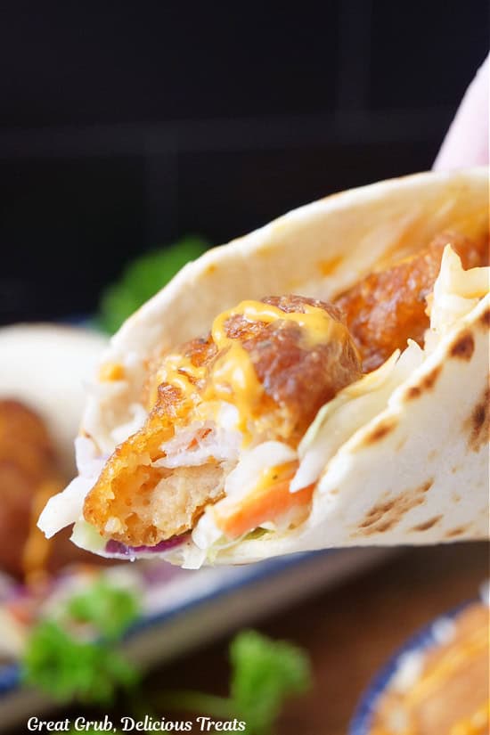 A shrimp taco with a bite taken out of a piece of fried shrimp.