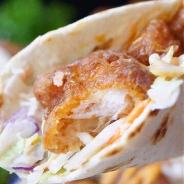 A shrimp taco with a bite taken out of it.