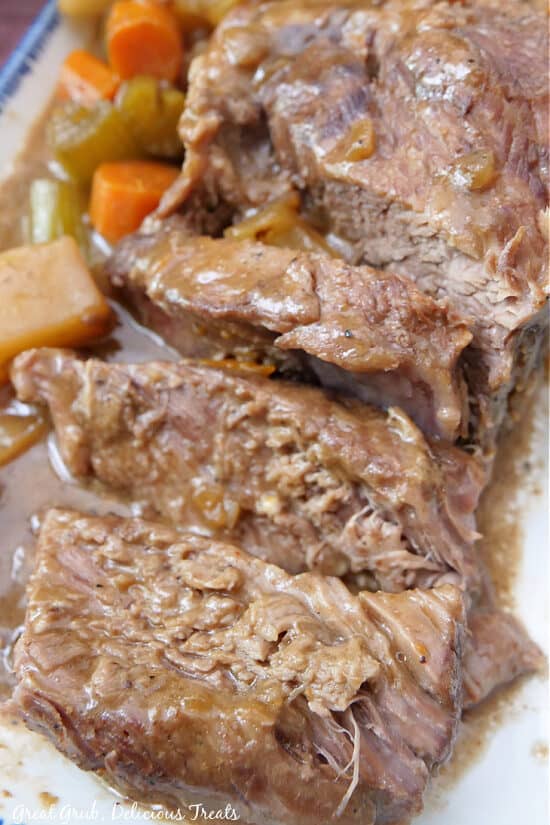 A close up of sliced chuck roast on a white plate with blue trim.