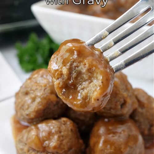 A meatball on a fork with a bite taken out of it, over a pile of meatballs on a white plate.