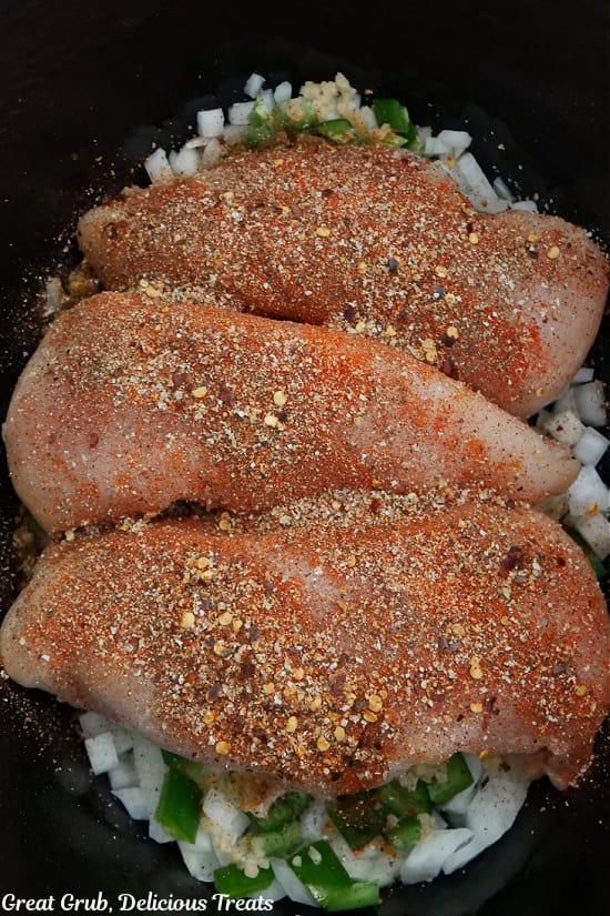 A crock pot with three seasoned uncooked chicken breasts.