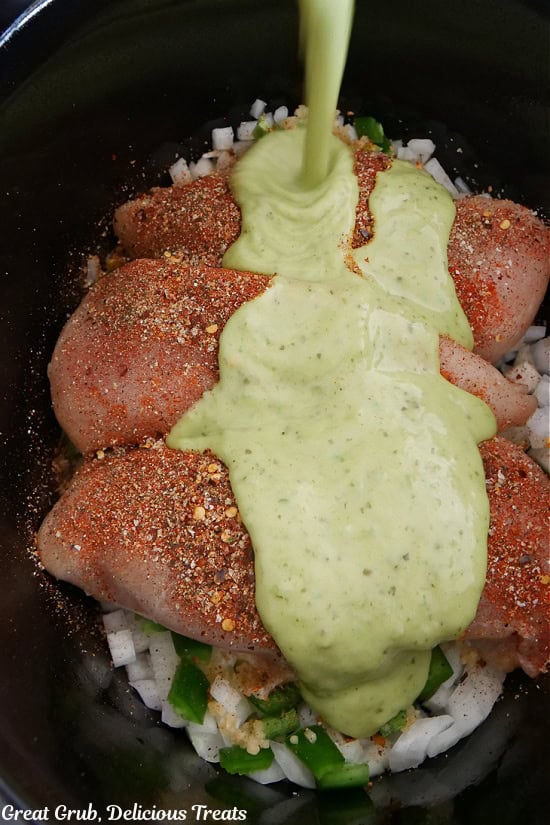 Three chicken breasts in the crock pot with a zesty guacamole salsa being poured on top of the chicken.
