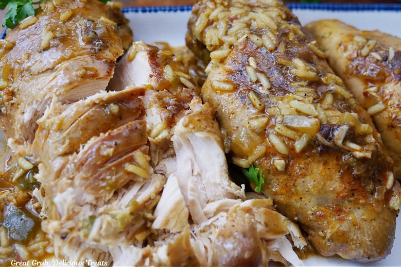 A white plate with blue trim with slow cooked chicken breasts and rice on it.