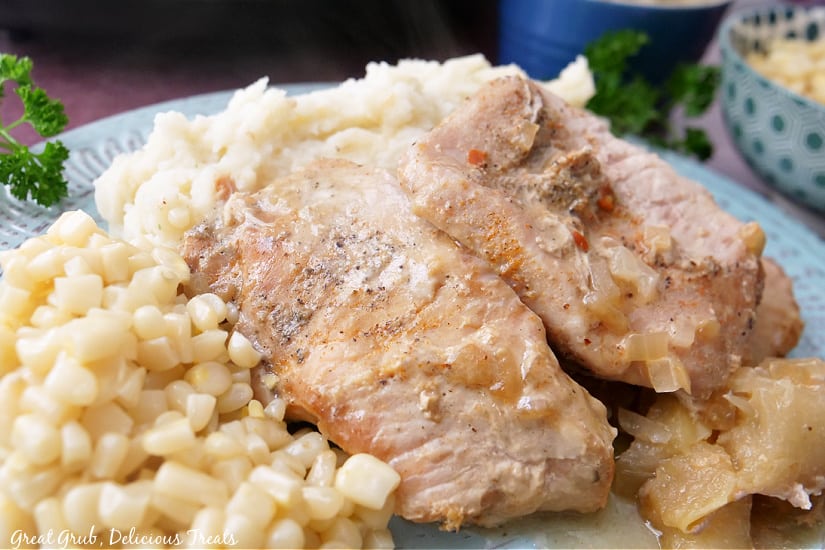 Slow Cooker Pork Chops with Apples is a delicious crock pot recipe that makes the most tender and flavorful pork chops. A landscape photo of a light blue plate with potatoes, corn, and pork chops.