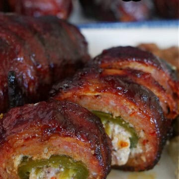 Two smoked armadillo eggs on a white plate with one of them sliced into bite size pieces.