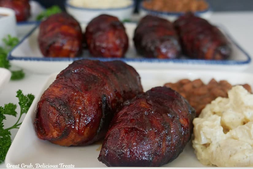 Two white plates with smoked bacon wrapped armadillo eggs on them.