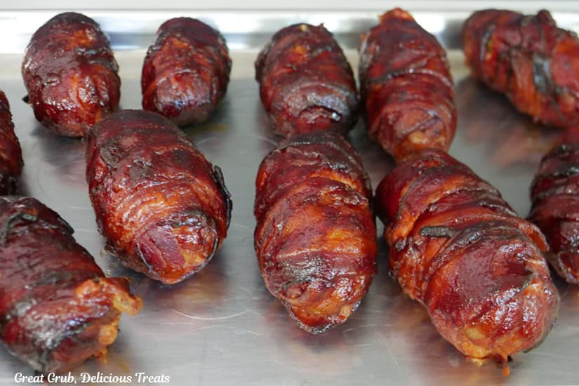 A silver baking sheet with 11 armadillo eggs that are bacon wrapped and smoked.