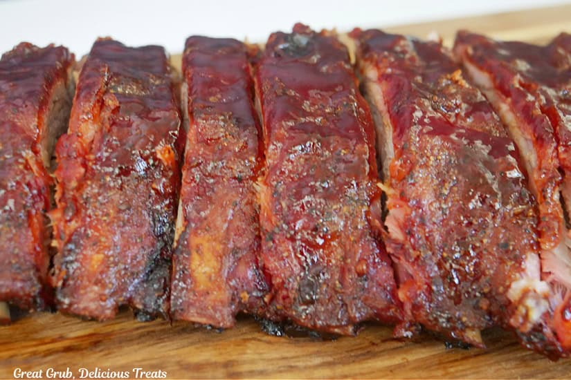 A wood cutting board with BBQ smoked ribs on it that have been sliced.