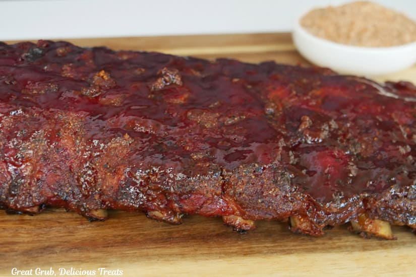 A rack of smoked pork ribs on a wood cutting board before being cut into individual ribs.
