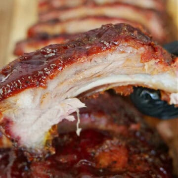 Smoked pork ribs on a wood cutting board with one rib held above the rack of ribs below.