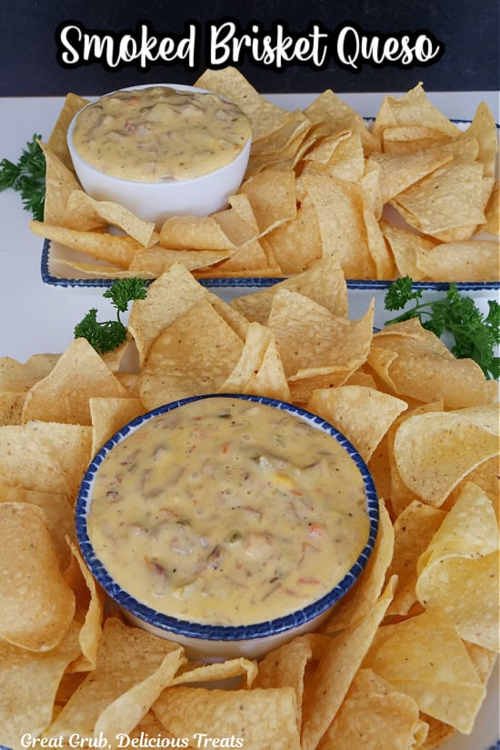 A white surface with two plates of tortilla chips and two bowls filled with homemade smoked brisket queso.
