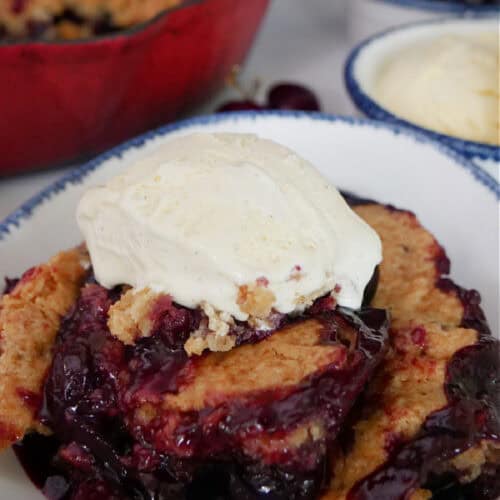 A white blue trimmed bowl with a serving of smoked cherry cobbler in it.
