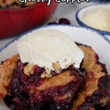 A white bowl with blue trim filled with a serving of smoked cherry cobbler with a scoop of vanilla ice cream on top.