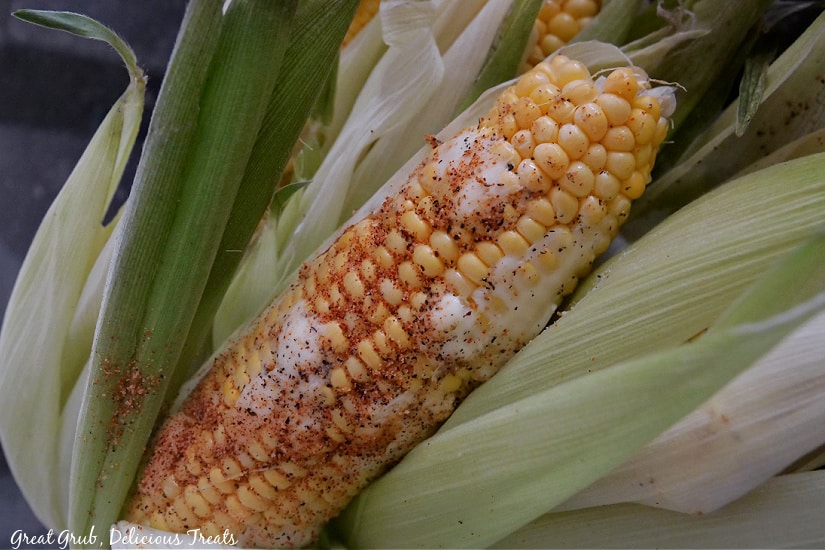 Corn on the cob with the husk, covered in butter and sprinkled with seasonings.