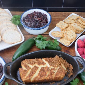 A wood surface with an oval black dish with a smoked cream cheese brick