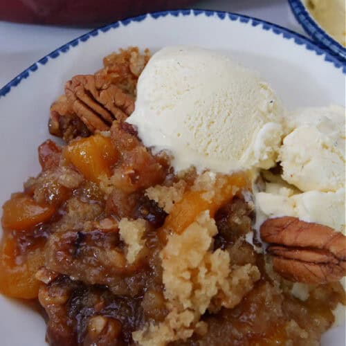 A white bowl with blue trim with a serving of peach cobbler in it with two scoops of ice cream.