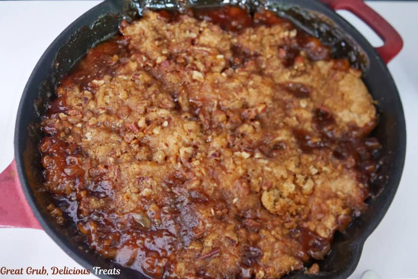 A white surface with a red and black cast iron skillet filled with smoked peach cobbler.