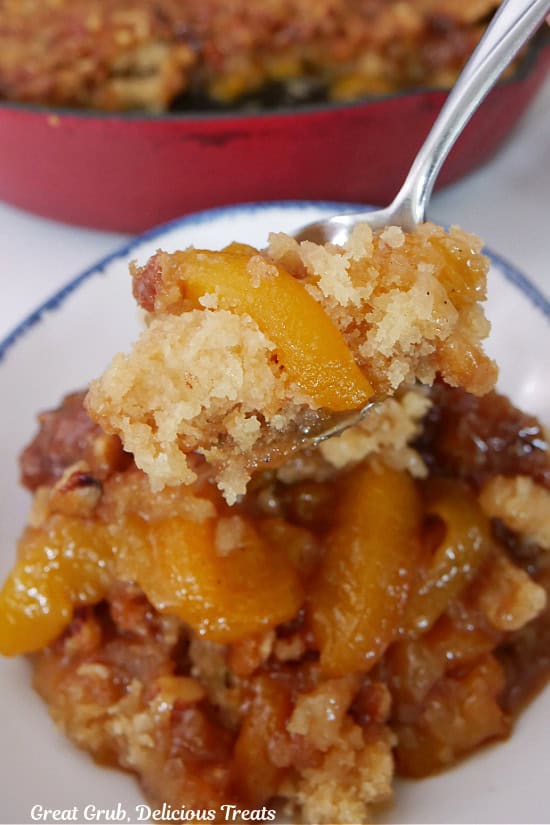 A white bowl with blue trim filled with a serving of peach cobbler and a spoon with a bite of cobbler on it.