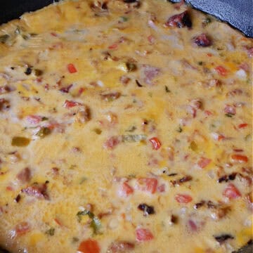 A red and black cast iron pan with smoked pulled pork queso in it.