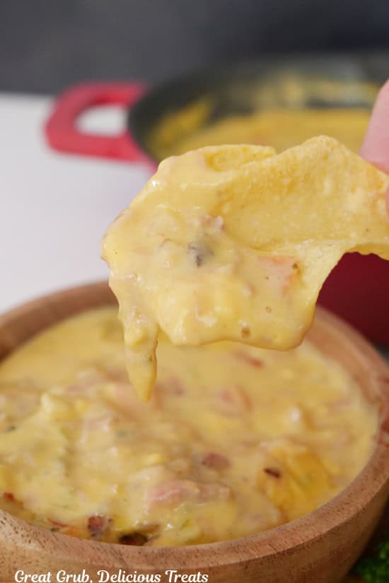 A small wood bowl with queso dip in it and a tortilla chip that has been dipped in the queso.