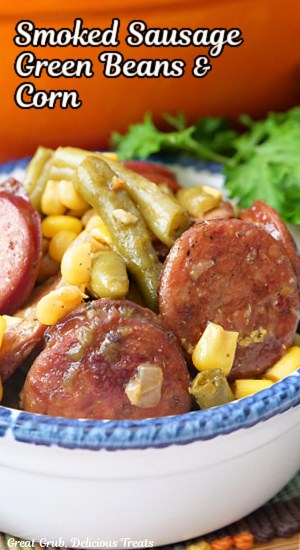 A white bowl with blue trim with a serving of sausage, green beans and corn in it.
