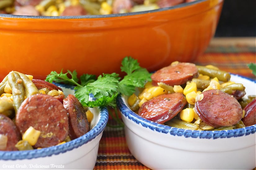 A horizontal photo of tow white bowls with blue trim filled with a serving of sausage, green beans