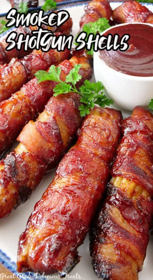A white plate with blue trim with stuffed manicotti shells wrapped in bacon and smoked with a small white bowl filled with barbecue sauce.