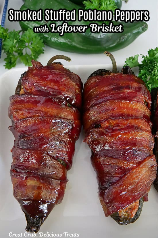 A white plate with two brisket stuffed poblano peppers that are wrapped in bacon and were smoked.