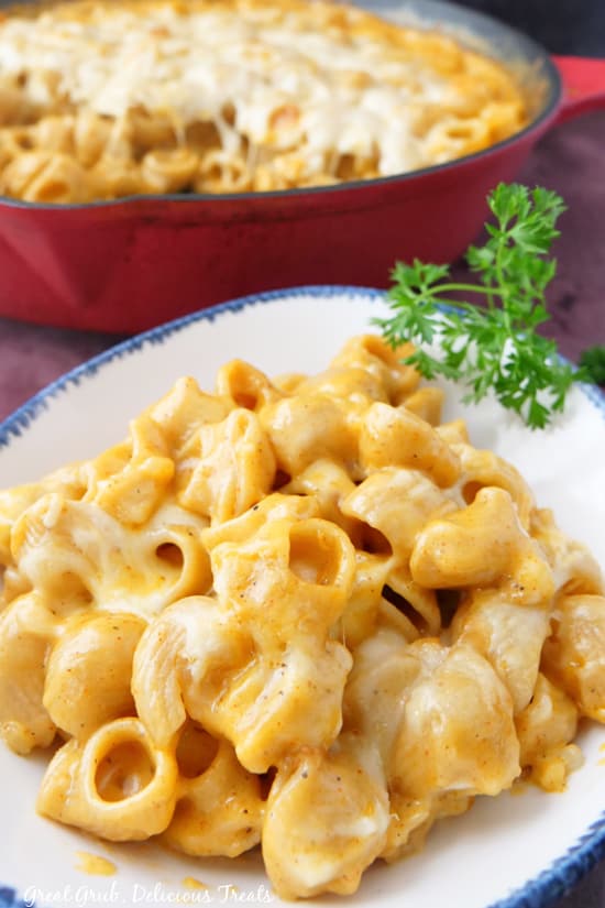 Smoked Mac and Cheese is a delicious mac and cheese recipe that is loaded with smoky flavors and lots of cheese. A white bowl filled with mac and cheese with a red cast iron full of mac and cheese in the background.