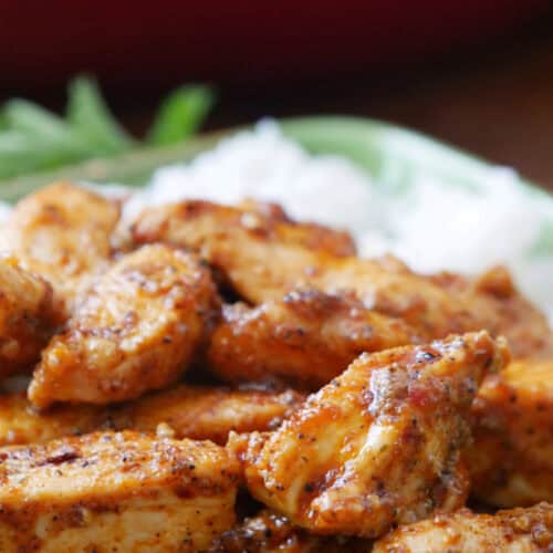 A close up of thin sliced Cajun chicken with white rice in the background.