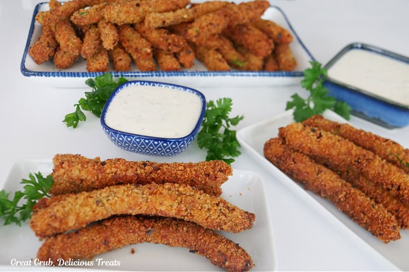 Three white plates fill ed with crispy deep fried green beans on them with two blue containers filled with ranch dressing.