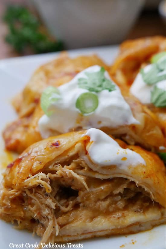 A chicken enchilada with the shredded chicken showing, and it is topped with sour cream and sliced green onions.