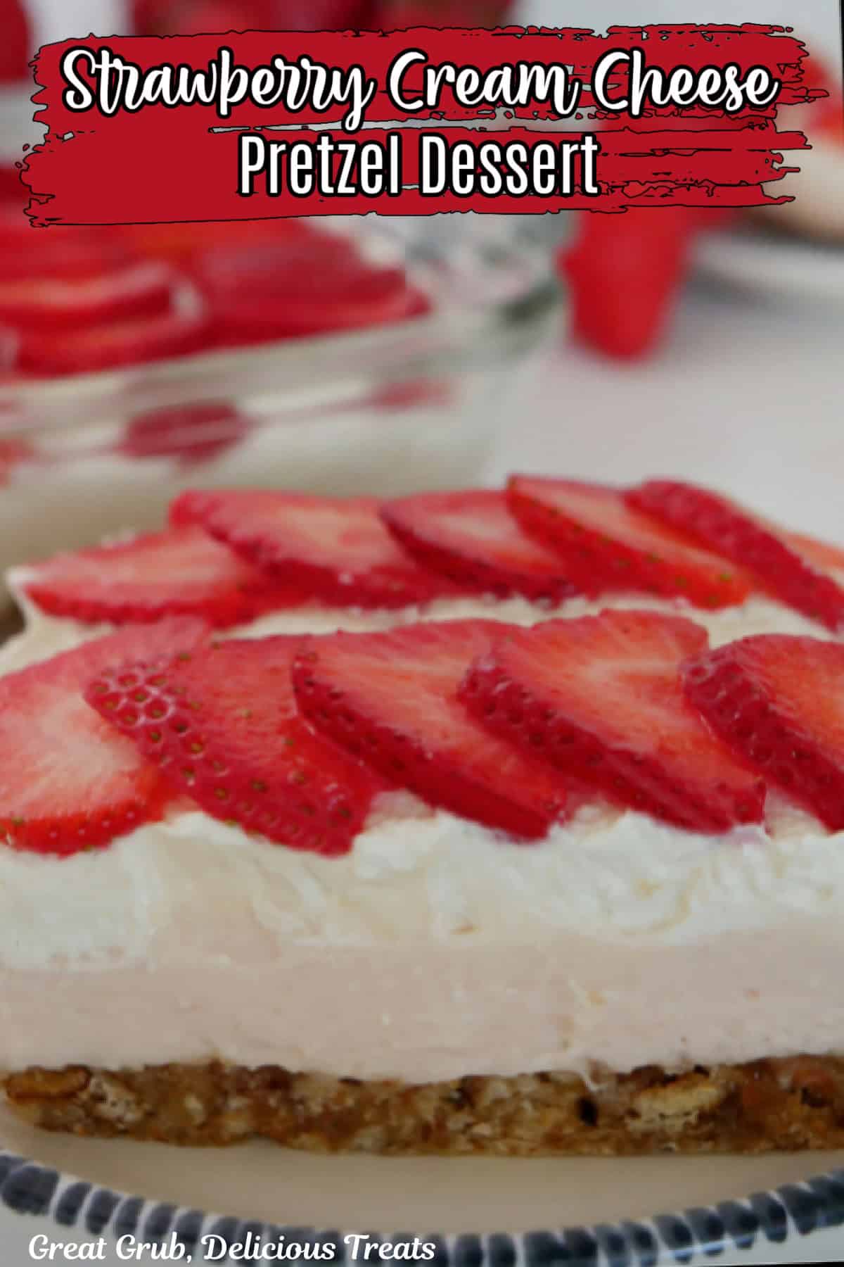 A round white plate with blue trim with a slice of strawberry pretzel dessert on it with fresh strawberries in the background.