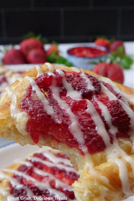 A strawberry danish held up to the camera with a few bites out of it.
