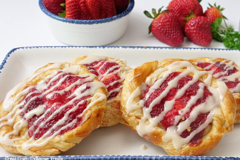 A horizontal photo of a white oblong plate with blue trim with four strawberry danishes on it.