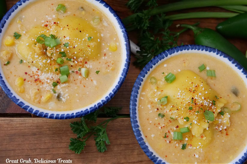 Two white bowls with blue trim, on a wood surface, filled with a serving of street corn ravioli soup.